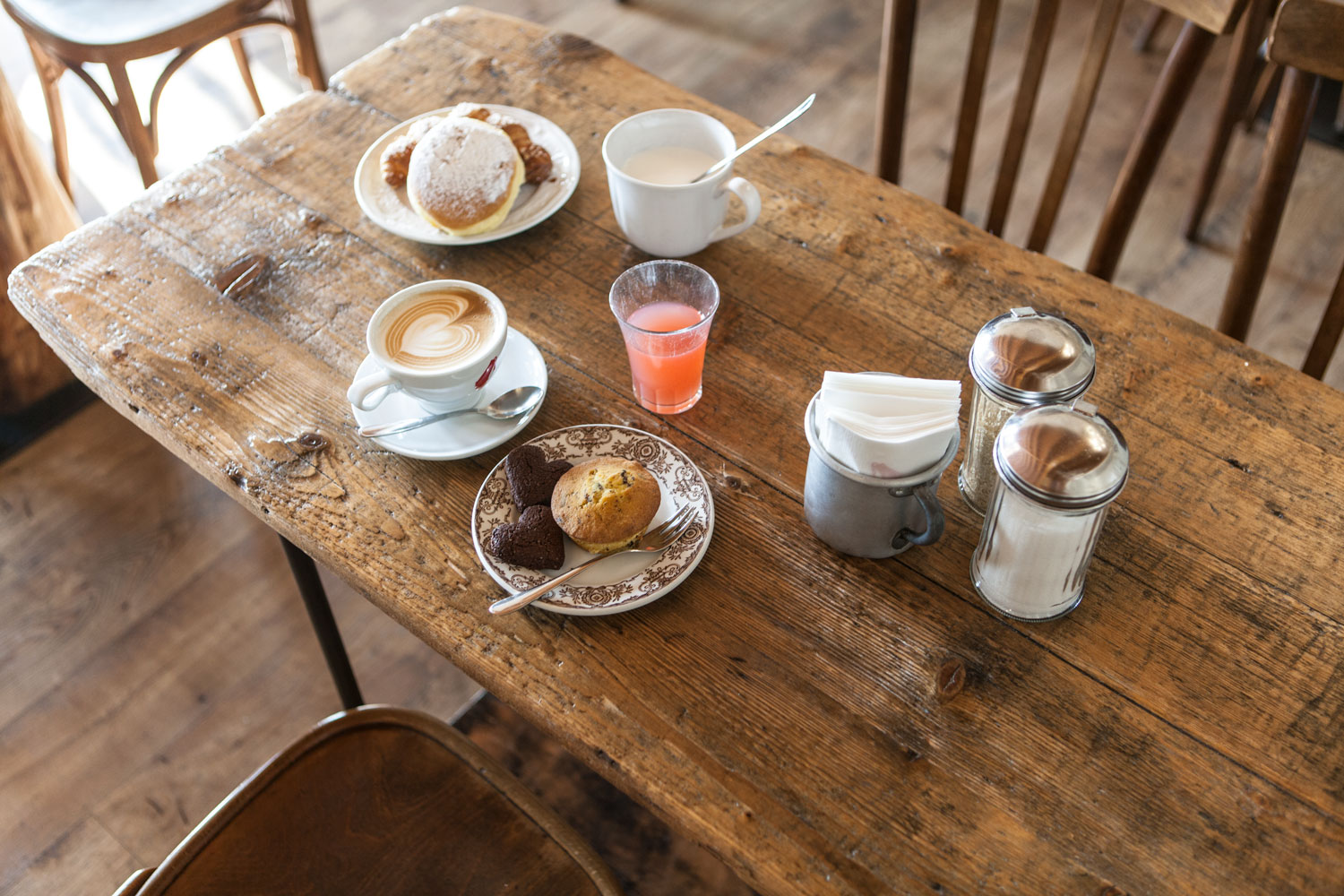 Tavolino in legno con cappuccini, spremuta, muffin e brioches